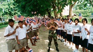 Dr. Patricia Steiner with Thai schoolchildren holding Thai and American flags at the Cobra Gold 2002 MEDCAP.